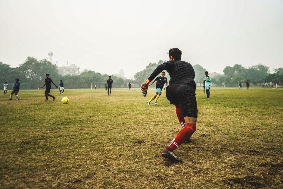 A soccer player in a black uniform and red socks is seen from behind, running on a grassy field during a game
